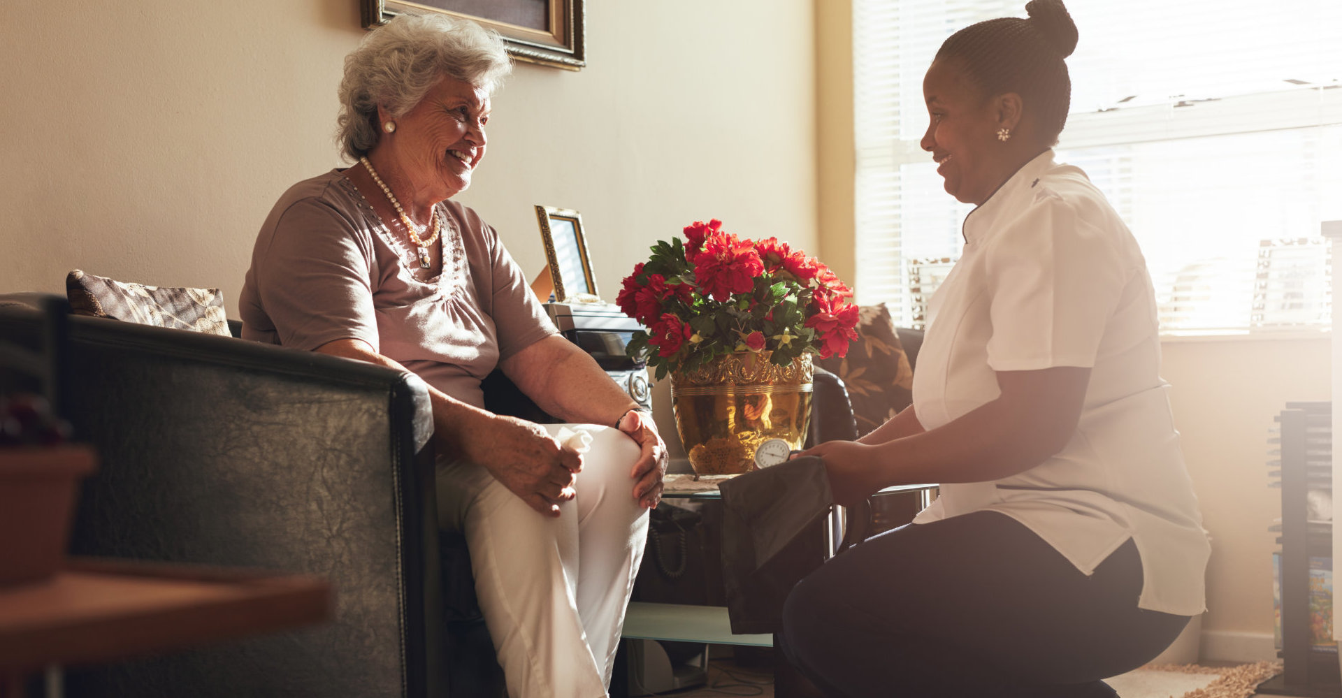 Senior woman sitting on a chair at home with female caregiver