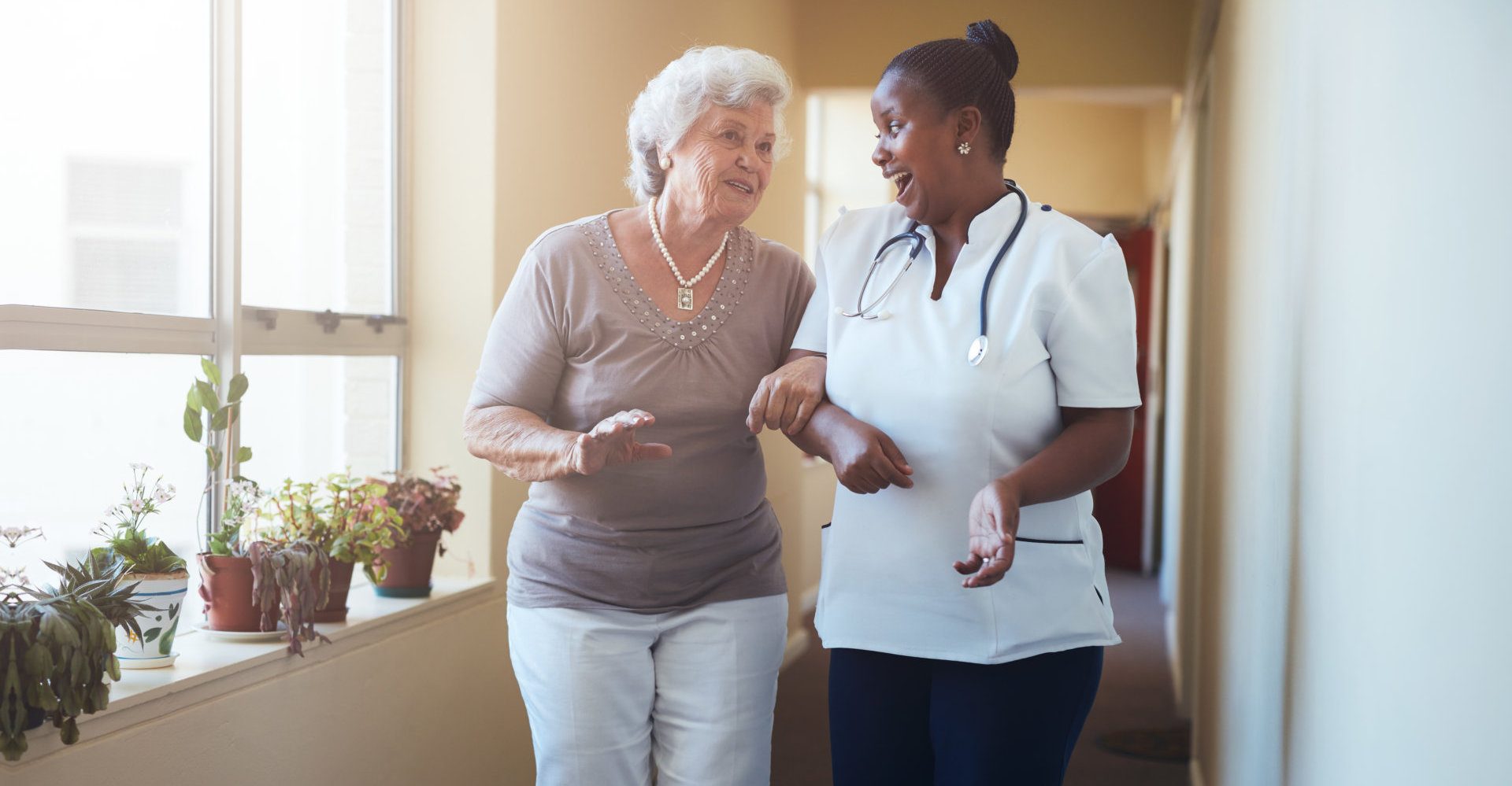 Portrait of happy healthcare worker walking and talking with senior woman